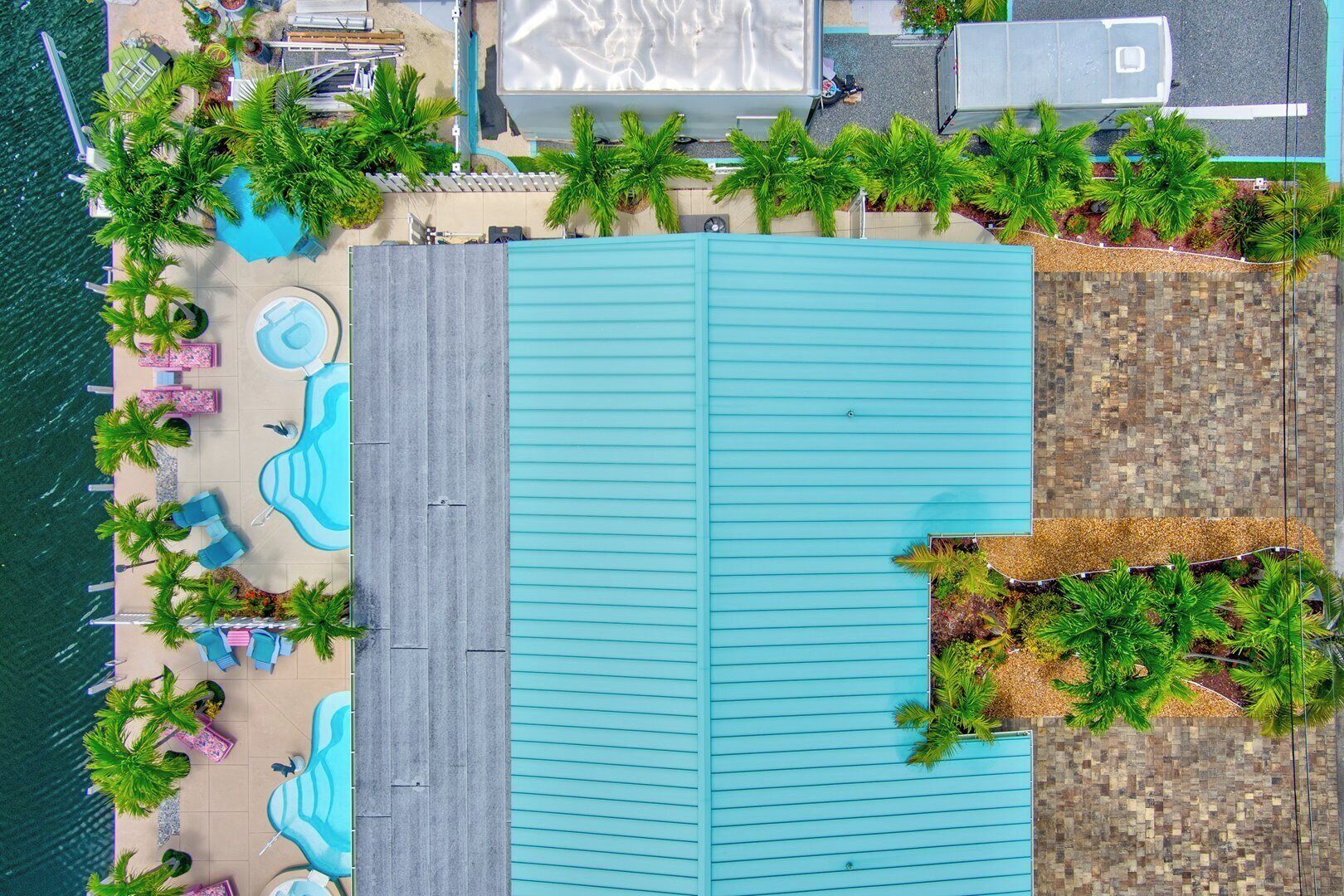An aerial view of a resort with a large swimming pool, lounge areas, and palm trees.