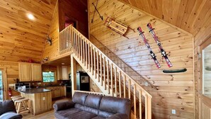 Ein gemütliches Blockhauss-Interieur mit einer Holztreppe, einem Ledersofa und Ski, die an der Wand hängen.