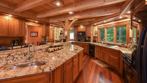 A spacious kitchen with wooden cabinets, granite countertops, and a large island with a sink. - Elegant Lakefront Retreat w/ Hot Tub & Fireplaces (Oakland)