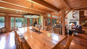 A spacious wooden dining area with a large table and chairs, a stone fireplace, and large windows overlooking a lake. - Elegant Lakefront Retreat w/ Hot Tub & Fireplaces (Oakland)