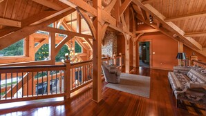 A spacious loft with wooden beams, a stone fireplace, and a view of the outdoors. - Elegant Lakefront Retreat w/ Hot Tub & Fireplaces (Oakland)