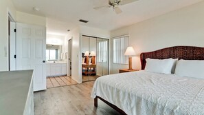 Un dormitorio con cama, mesita de noche, lámpara y vistas al baño.