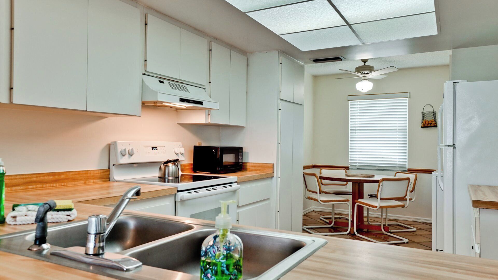 A compact kitchen with a stove, microwave, and sink. There is a dining area with a table and chairs.
