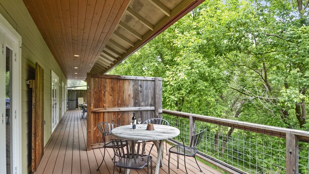 Une terrasse en bois avec une table ronde et des chaises, une clôture en bois et une vue sur des arbres verdoyants.