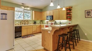 Une cuisine avec des meubles de rangement en bois, un îlot central doté de tabourets, un réfrigérateur et un four à micro-ondes.