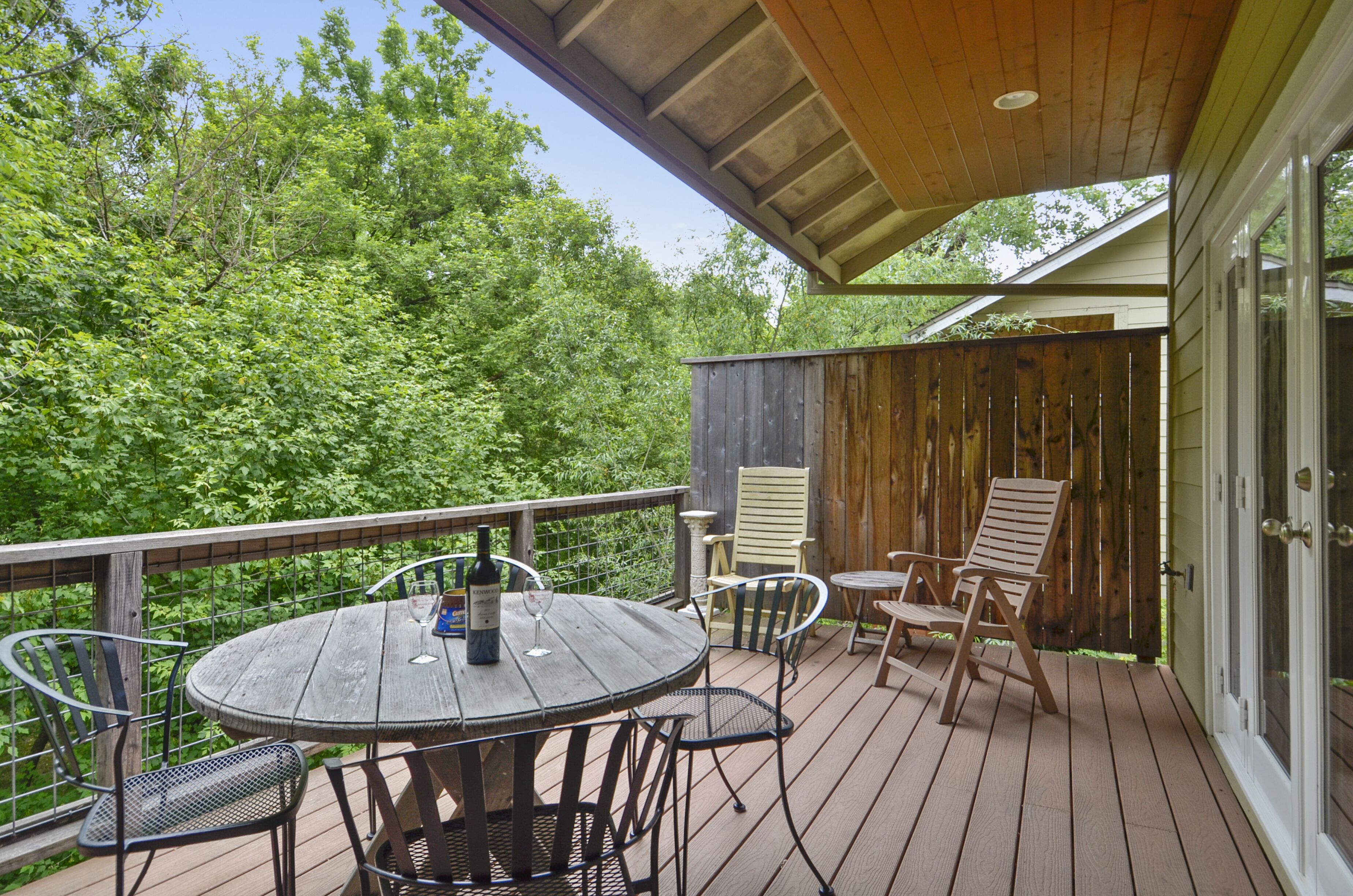 A wooden deck with a round table and chairs, a bottle of wine, and a glass on the table.