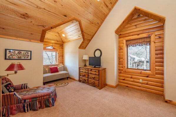 A cozy log cabin interior with a sofa, a TV, and a fireplace. - Charming Lodge w/ Pool Table, Bar & Fireplaces (SWANTON)