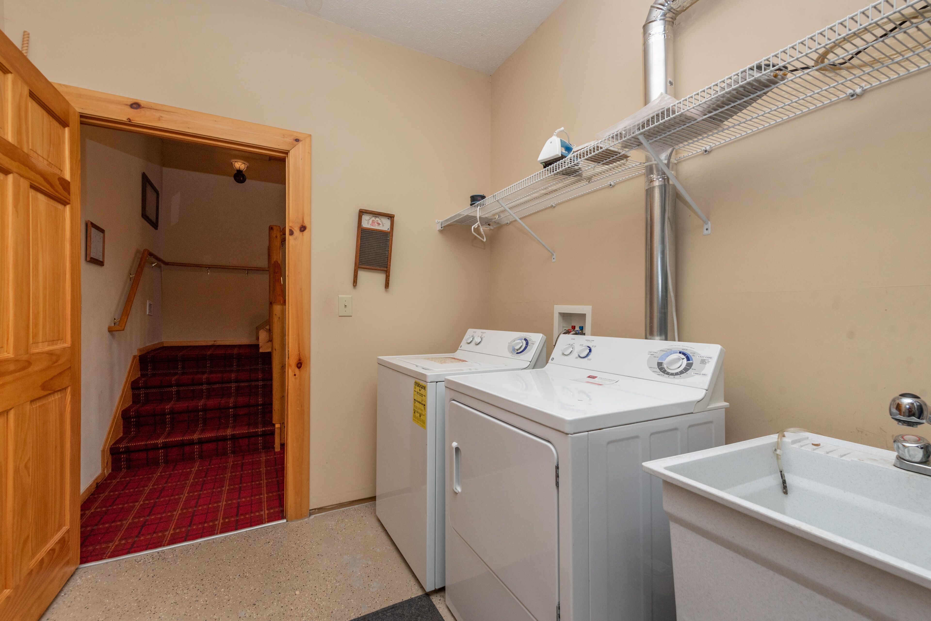 A laundry room with two washing machines, a drying rack, and a sink.