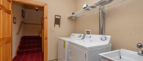 A laundry room with two washing machines, a drying rack, and a sink.
