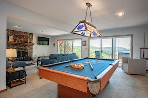 Une table de billard, un luminaire suspendu, une cheminée et une vue sur l’extérieur.