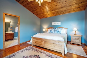 Un dormitorio con techo de madera, una cama con ropa de cama floral, una mesita de noche con lámpara y un espejo con luces.