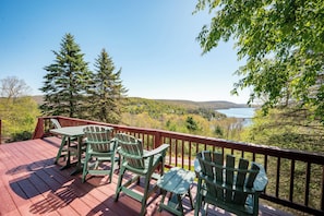 A wooden deck with chairs and a table overlooking a lake and forest.