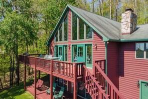A cabin with a deck, large windows, and a stone chimney.
