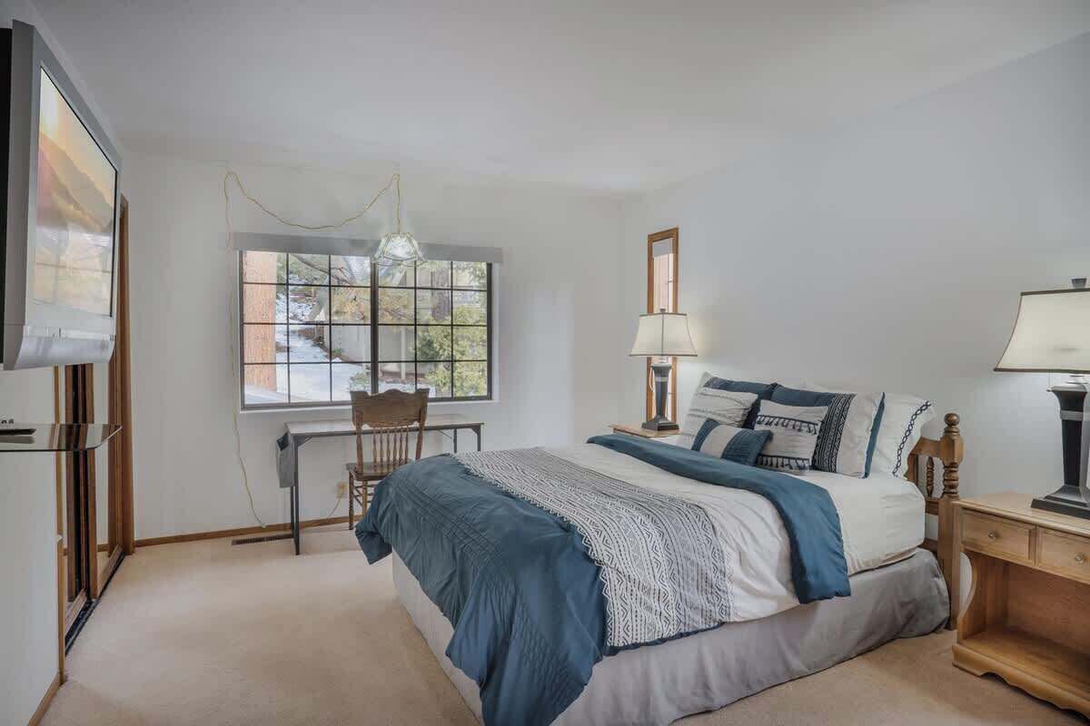 Un dormitorio con cama, mesitas de noche, escritorio, silla y ventana.