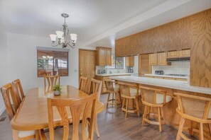 A modern kitchen with wooden cabinets, a central island, and a dining area with wooden chairs.