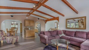 Un vaste espace de vie comprenant un grand canapé, une table basse en verre et des poutres en bois au plafond.