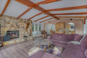 A living room with a stone wall, wooden beams, a fireplace, a purple sofa, and a glass coffee table.