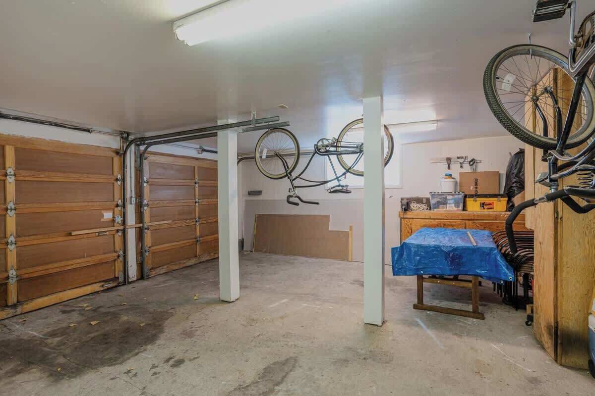 A garage with two wooden garage doors, a bicycle hanging from the ceiling, and a workbench with a blue tarp.