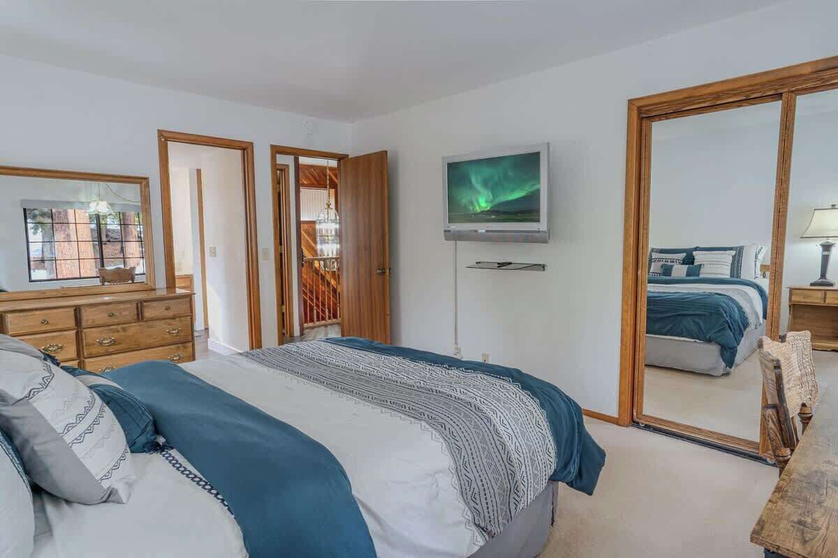 A bedroom with a bed, dresser, TV, and a large mirror.