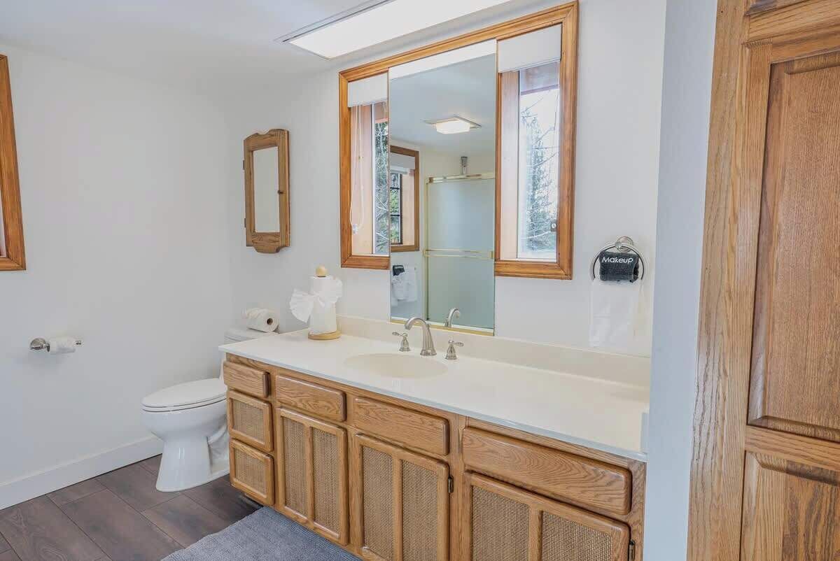 Un bagno con un WC bianco, un mobile bagno in legno con specchio e un lavandino.