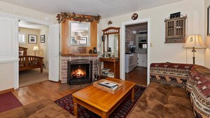 Ein gemütliches Wohnzimmer mit Kamin, einer Couch, einem Couchtisch und einer Küche im Hintergrund.