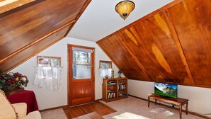 Ein gemütliches Dachzimmer mit schrägen Wänden, einem Holzregal, einem Fernseher und einem kleinen Tisch.