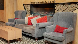 A cozy seating area with three grey armchairs, a wooden coffee table, and a fireplace with logs. - Comfort Suites Tokyo Bay (Urayasu)