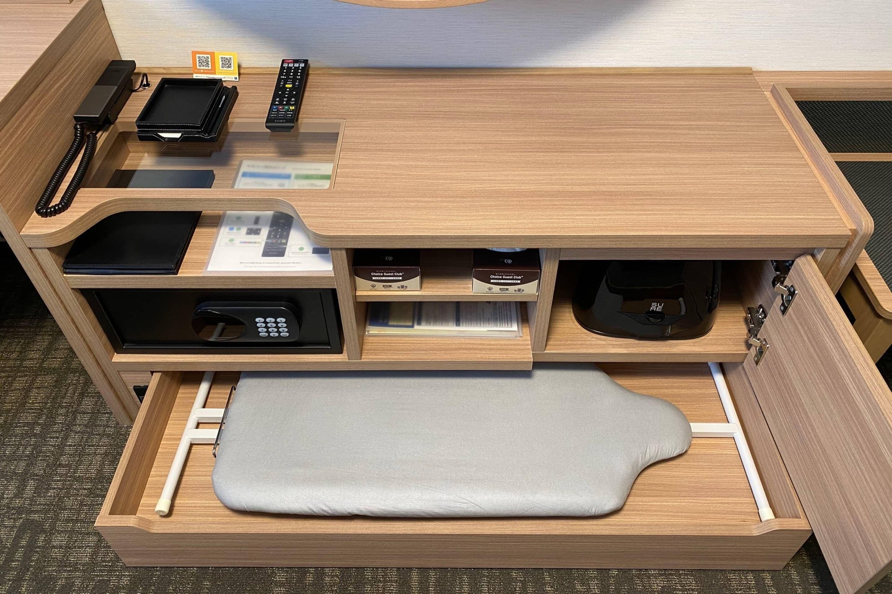 Un escritorio de madera con teléfono integrado, controles remotos, una mesita pequeña y compartimentos de almacenamiento.