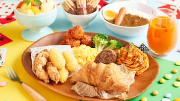 A meal with various dishes on a wooden plate, including fried items, vegetables, and a glass of orange juice.