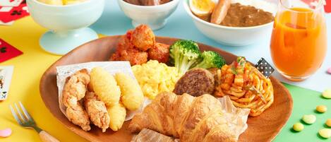 A meal with various dishes on a wooden plate, including fried items, vegetables, and a glass of orange juice.