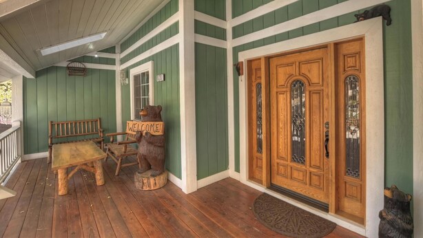 A wooden porch with a bench, a welcome sign, and a large wooden door with glass panels. - HOT TUB! PET FRIENDLY! Two Game Rooms! Propane BBQ! Log Furnishings! WiFi! (Big Bear City)