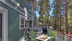 A wooden deck with a fire pit, green chairs, and a white railing. - HOT TUB! PET FRIENDLY! Two Game Rooms! Propane BBQ! Log Furnishings! WiFi! (Big Bear City)