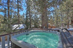 Un bain à remous entouré de grands pins et doté d’une terrasse en bois.