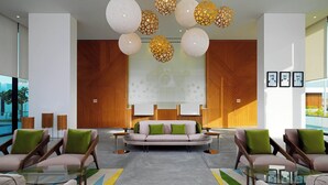 Un hall d’entrée moderne avec un canapé central, deux fauteuils, une table basse en verre et des lampes décoratives en forme de sphère.