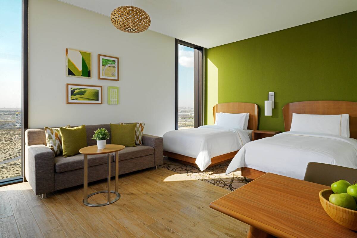 Ein modernes Hotelzimmer mit zwei Betten, einer Couch, einem kleinen Tisch und Blick auf die Stadt.