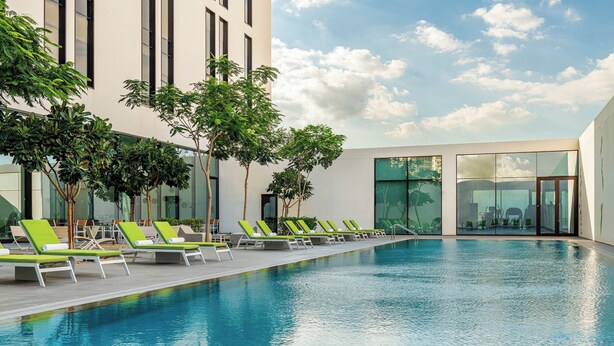 Une piscine avec des chaises longues, un bâtiment moderne doté de grandes fenêtres et un ciel dégagé.