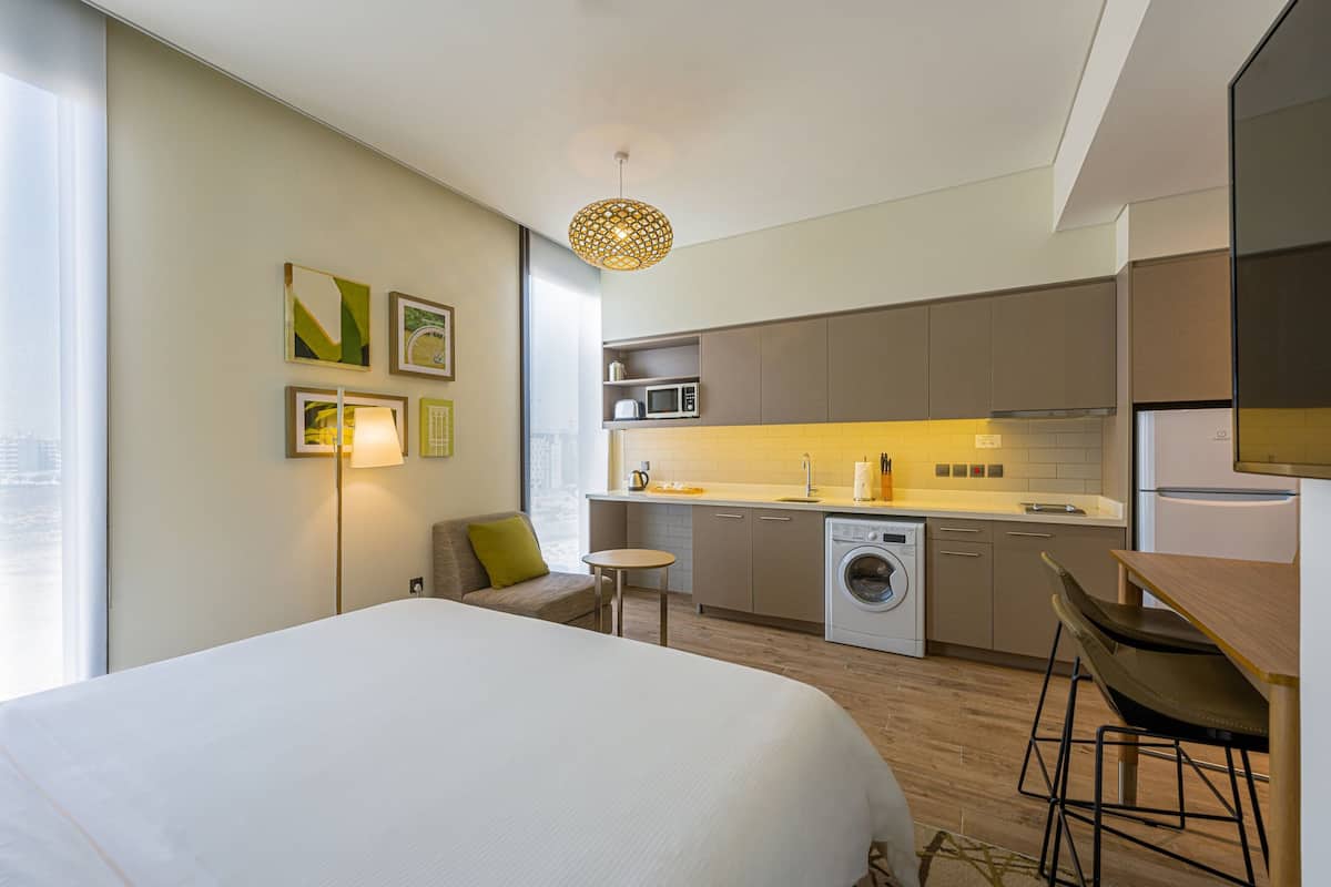 Ein modernes Hotelzimmer mit einem großen Bett, einer kleinen Küchenzeile, einer Waschmaschine und einem Essbereich.