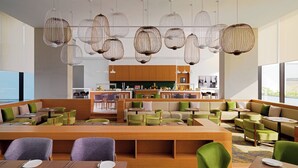Un restaurant moderne doté d’un espace central avec des sièges, de nombreuses tables et des luminaires suspendus.
