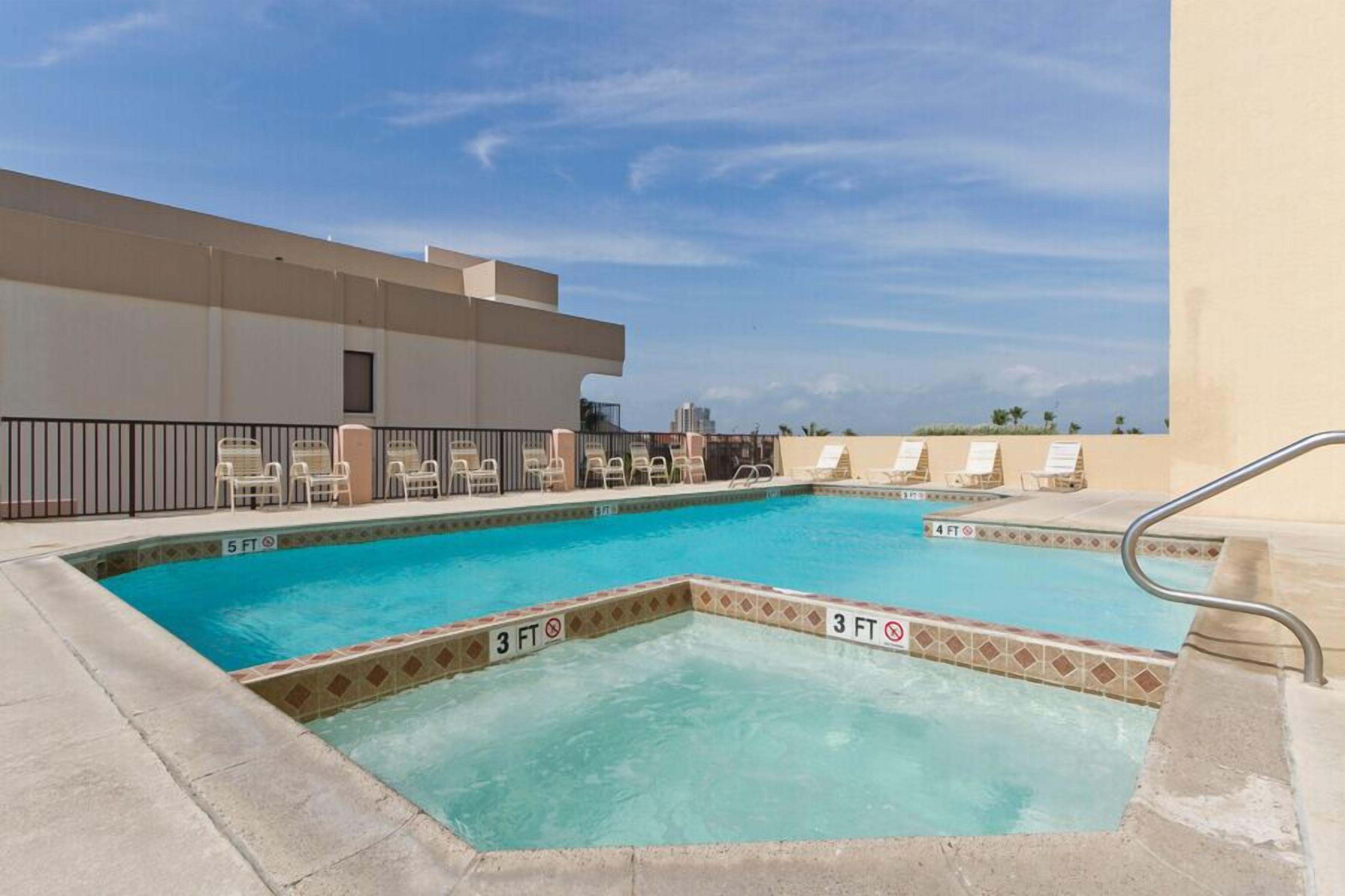 A rooftop pool with a 5 FT depth marker, lounge chairs, and a clear sky.
