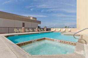 A rooftop pool with clear blue water, surrounded by lounge chairs and a low fence.