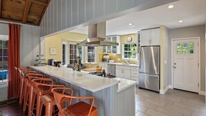 Une cuisine moderne dotée d’un grand îlot central, de tabourets de bar, d’appareils électroménagers en acier inoxydable et offrant une vue sur l’extérieur.