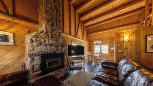A cozy log cabin interior with a stone fireplace, leather sofa, and wooden dining table. - Log Cabin on Slate River | 4 Bedroom | Mt CB View | River Access (Crested Butte)