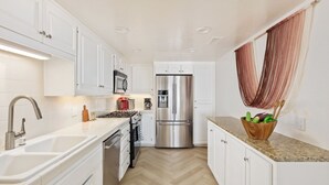 Una cocina moderna con armarios blancos, electrodomésticos de acero inoxidable y piso de madera con patrón de espiga.