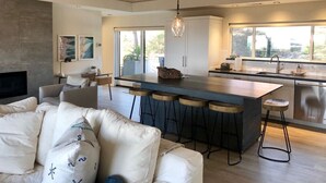 A modern kitchen with a central island, bar stools, and a large window providing natural light. - Luxury 2 Bed/2 Bath Penthouse in Shell Beach, Overlooking the Coast with Wrap-Around Balconies (Shell Beach)