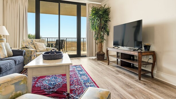 Un soggiorno con divano, tavolino, televisore, un'ampia finestra e un balcone.