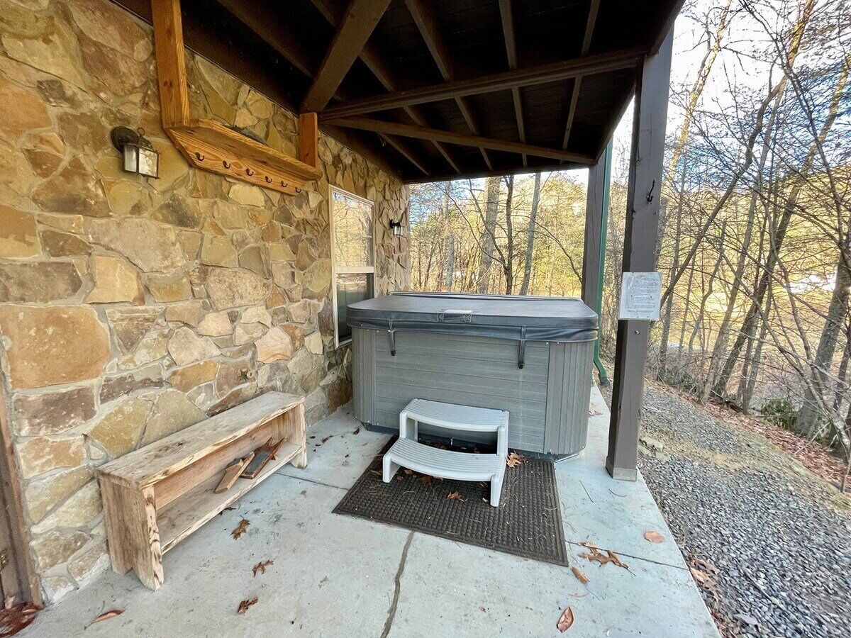 A stone-walled outdoor area with a hot tub, a wooden bench, and a small step for accessibility.
