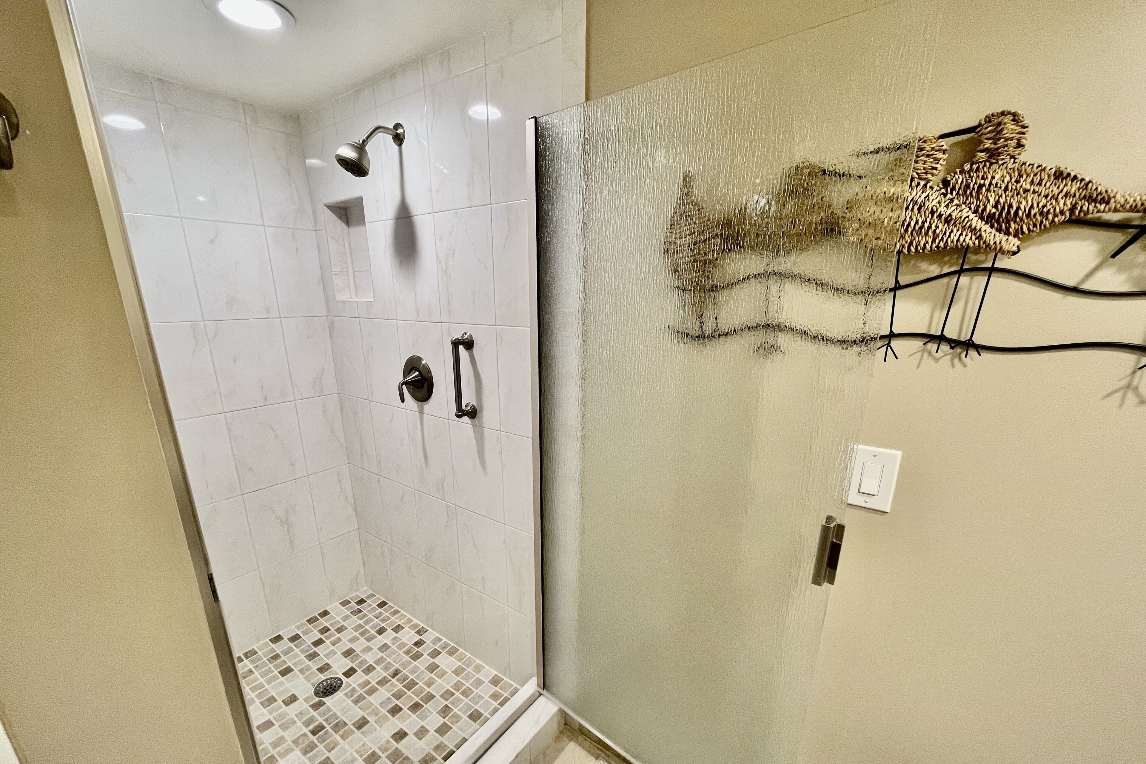 Une douche avec une porte en verre, un porte-serviettes fixé au mur et un sol carrelé.