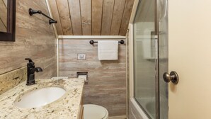 Une salle de bain avec un plafond en bois, un lavabo avec un robinet, des toilettes et un espace douche doté d’une porte en verre.