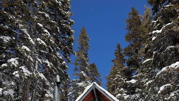 Une cabane au toit en pente, entourée d’arbres couverts de neige.