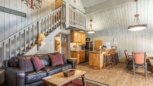 Un salon chaleureux avec un canapé en cuir, une table basse en bois et un escalier menant à un niveau supérieur.